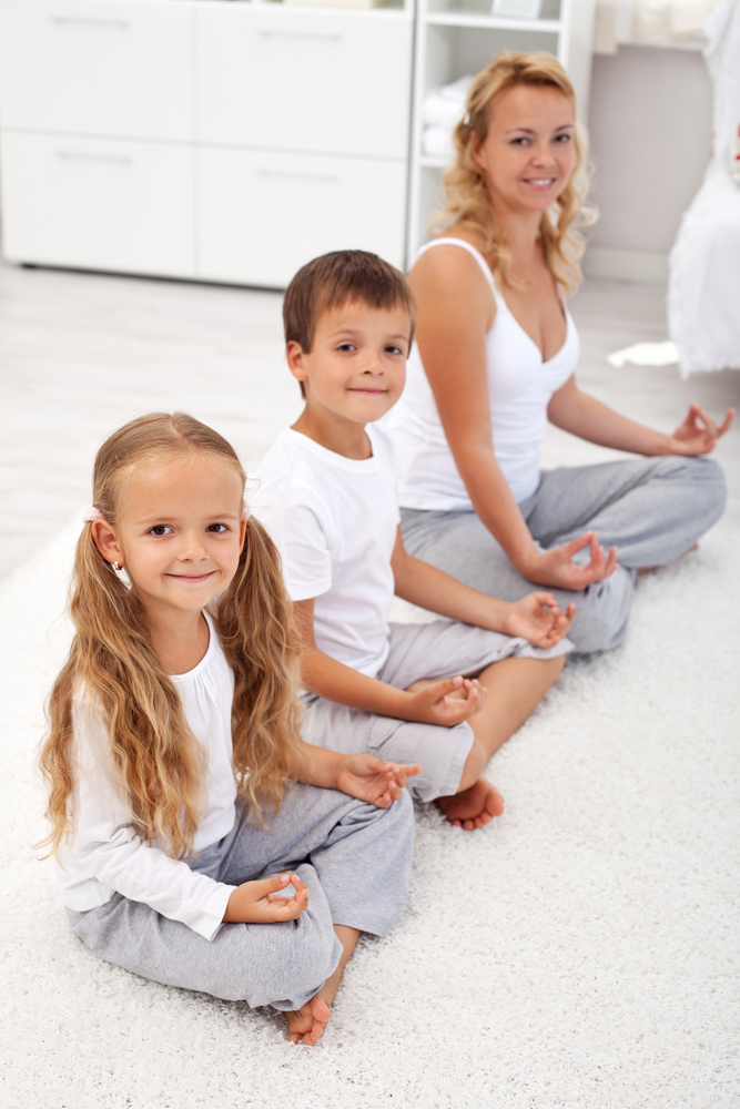 Happy smiling kids doing yoga relaxation at home with their mother - focus on the little girl