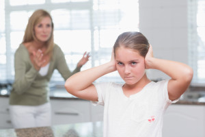 Upset little girl covering her ears while her mother screaming at home in the kitchen