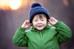 Cute little boy, holding his hands over ears not to hear, making sweet funny face